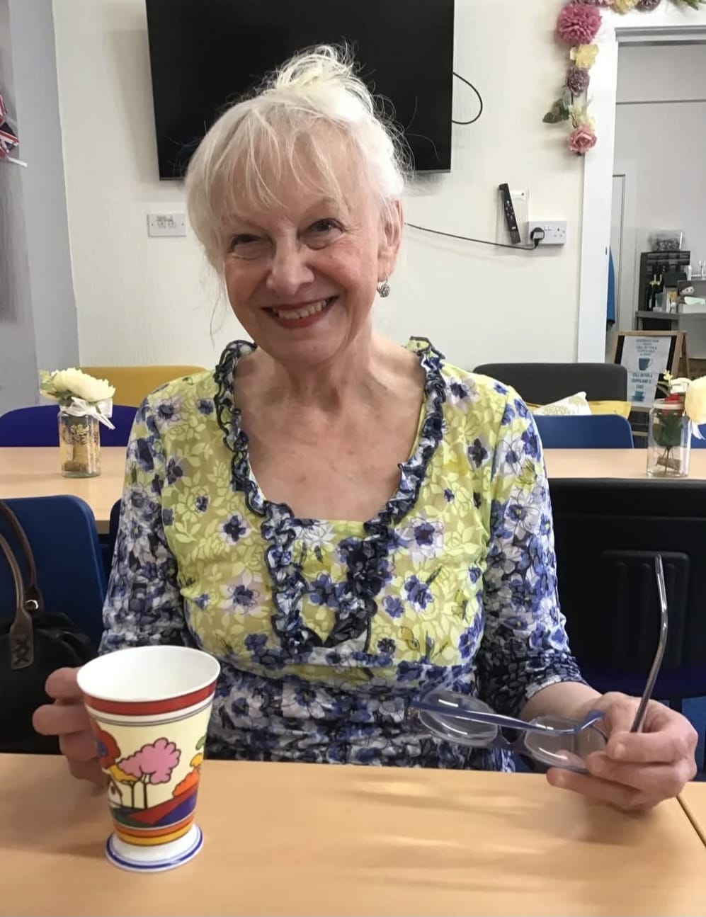 A smiling Sylvia Edwards sitting at a desk with a cup of tea.